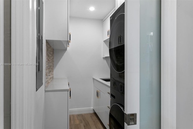 clothes washing area with cabinets, stacked washer / drying machine, and hardwood / wood-style floors