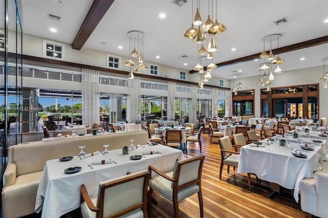 dining area featuring beamed ceiling, light hardwood / wood-style floors, and a high ceiling