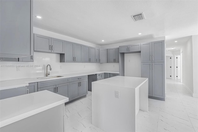 kitchen with a textured ceiling, a center island, gray cabinetry, and sink