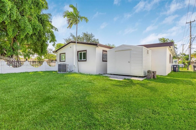 rear view of property featuring a lawn, cooling unit, and a storage shed