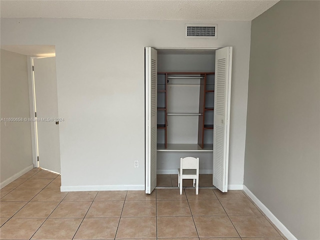 unfurnished bedroom featuring a textured ceiling, a closet, and light tile floors