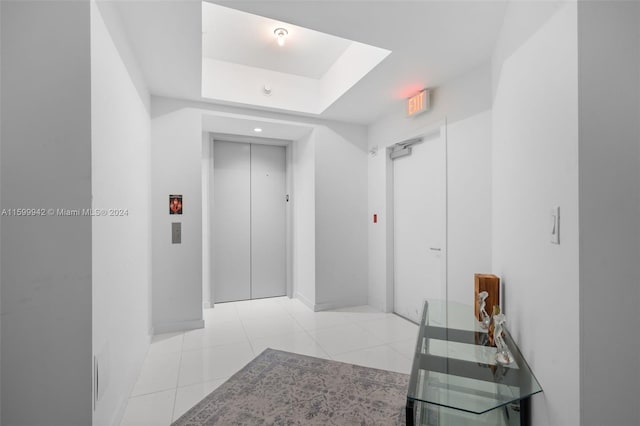 hallway with light tile patterned floors, a tray ceiling, and elevator