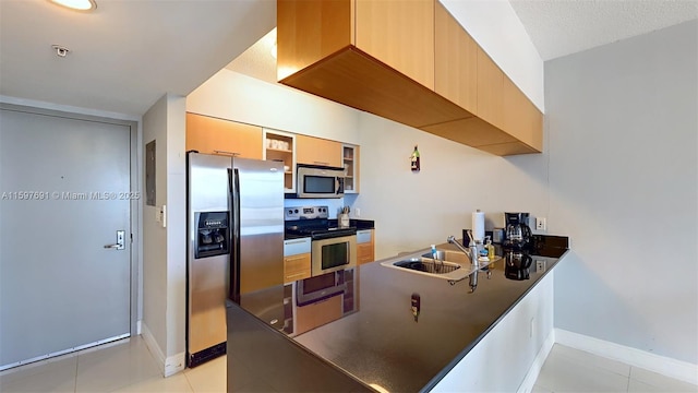 kitchen with a sink, dark countertops, appliances with stainless steel finishes, a peninsula, and light tile patterned floors