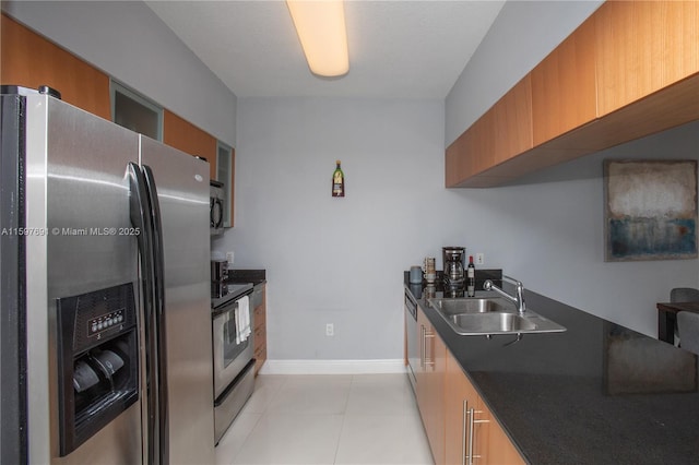 kitchen featuring brown cabinets, a sink, dark countertops, appliances with stainless steel finishes, and light tile patterned floors