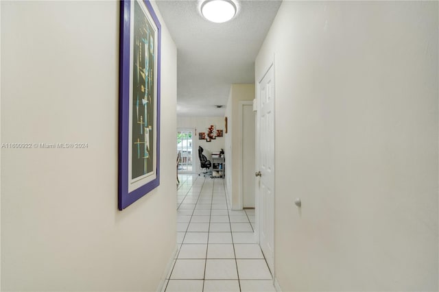 corridor with a textured ceiling and light tile floors