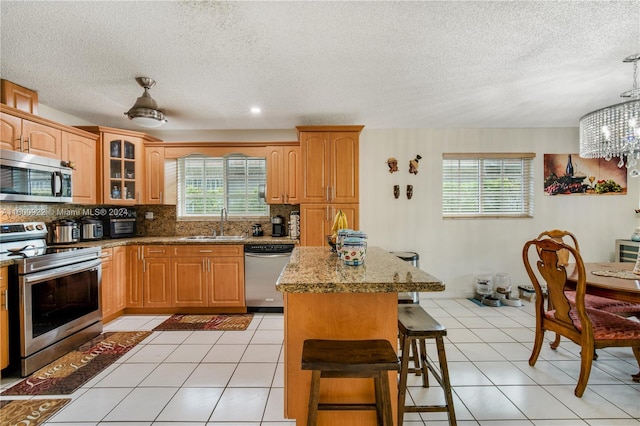 kitchen with appliances with stainless steel finishes, backsplash, light tile flooring, and pendant lighting