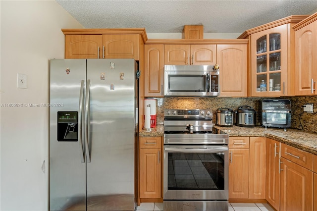 kitchen featuring light stone counters, light tile flooring, stainless steel appliances, tasteful backsplash, and a textured ceiling