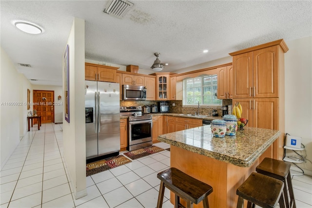 kitchen featuring tasteful backsplash, appliances with stainless steel finishes, sink, light tile floors, and a breakfast bar