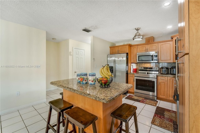 kitchen with a kitchen island, stainless steel appliances, a breakfast bar, tasteful backsplash, and light tile flooring