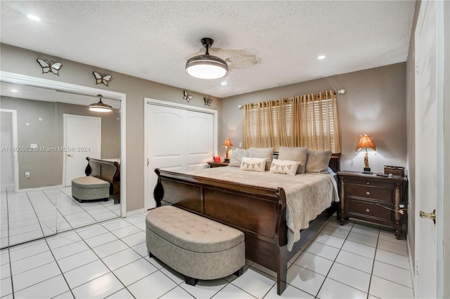 bedroom featuring ceiling fan, a closet, a textured ceiling, and light tile floors