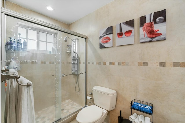 bathroom featuring a shower with shower door, toilet, and tile walls