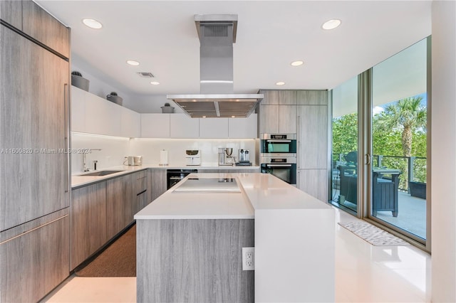 kitchen featuring double oven, a kitchen island, island range hood, sink, and light tile floors