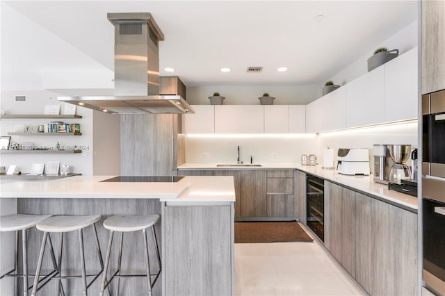 kitchen featuring island range hood, a kitchen breakfast bar, beverage cooler, and white cabinetry