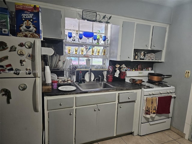 kitchen featuring dark countertops, a sink, light tile patterned flooring, white appliances, and open shelves