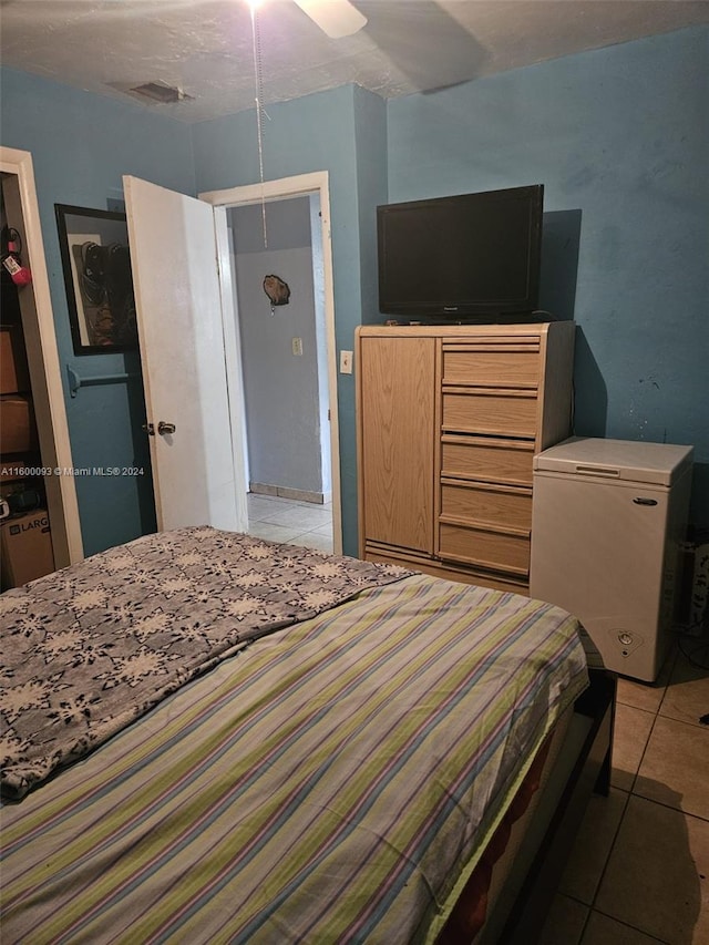 bedroom with light tile patterned floors, visible vents, fridge, and ceiling fan
