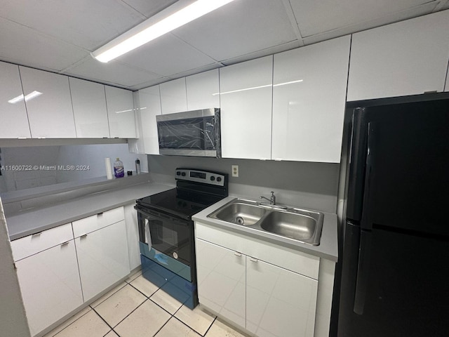 kitchen featuring range with electric stovetop, sink, light tile patterned floors, white cabinetry, and black fridge