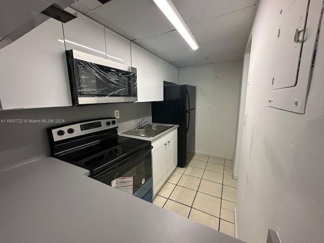 kitchen featuring sink, light tile patterned floors, black refrigerator, range with electric cooktop, and white cabinets