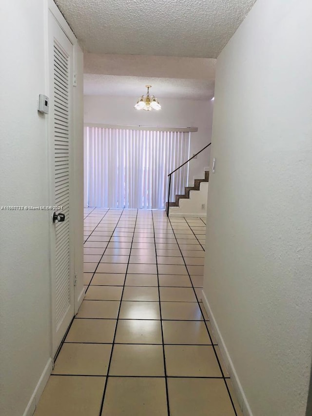 hallway featuring tile patterned floors, a chandelier, and a textured ceiling