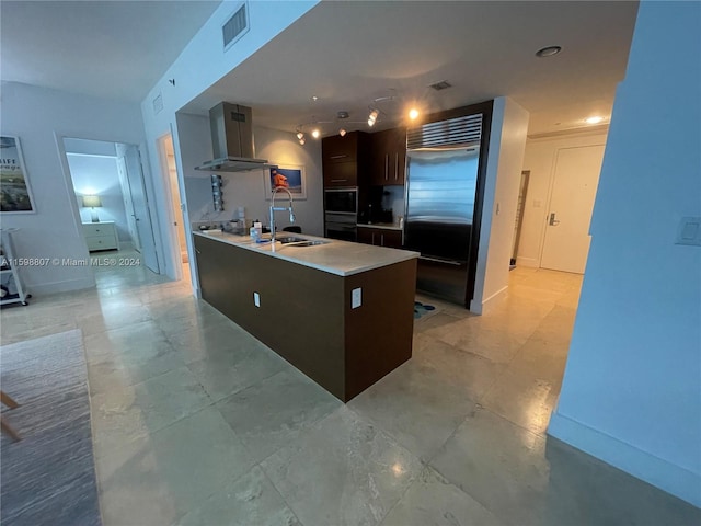 kitchen featuring wall chimney exhaust hood, built in fridge, light tile patterned floors, sink, and dark brown cabinets