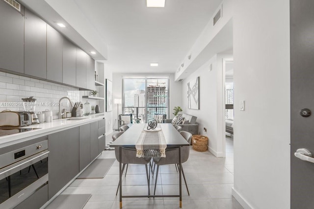 kitchen featuring sink, gray cabinetry, backsplash, stainless steel oven, and a breakfast bar area