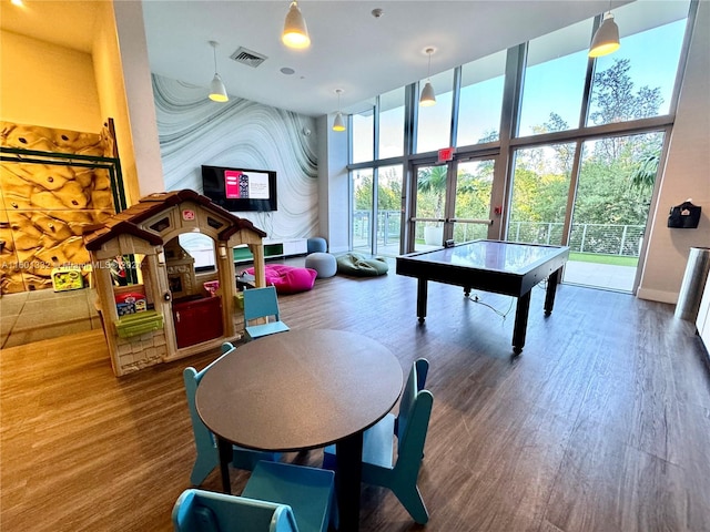 game room with floor to ceiling windows, a towering ceiling, and wood-type flooring