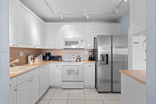 kitchen with white cabinets, white appliances, light tile patterned floors, a textured ceiling, and sink