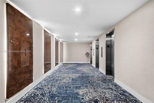 hall featuring carpet floors, baseboards, and elevator