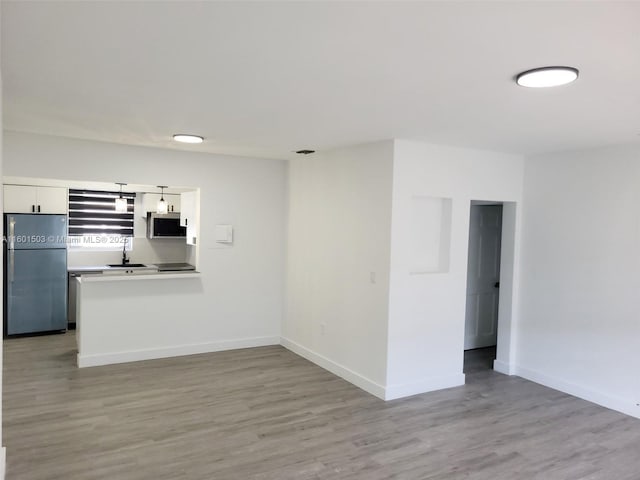 interior space with appliances with stainless steel finishes, sink, light hardwood / wood-style flooring, white cabinets, and hanging light fixtures