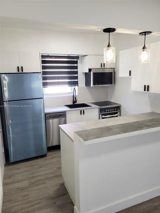 kitchen with appliances with stainless steel finishes, dark hardwood / wood-style flooring, sink, decorative light fixtures, and white cabinets