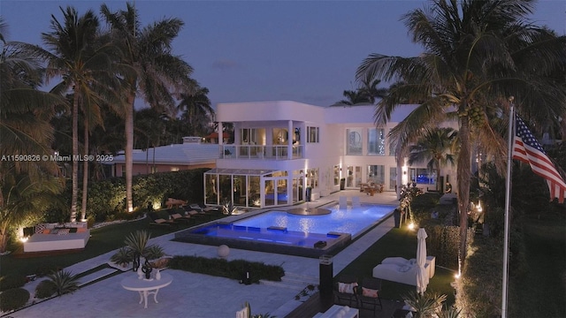 back house at dusk with a patio area, a balcony, and a swimming pool with hot tub