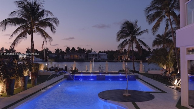 pool at dusk with pool water feature, a water view, and a patio area