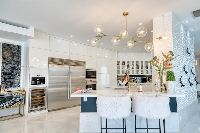 kitchen featuring a breakfast bar, built in appliances, decorative light fixtures, white cabinetry, and wine cooler