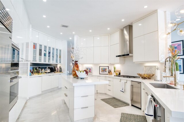 kitchen with white cabinets, sink, wall chimney exhaust hood, appliances with stainless steel finishes, and a kitchen island