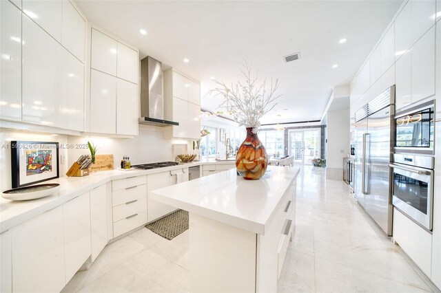 kitchen with built in appliances, white cabinets, wall chimney range hood, and sink