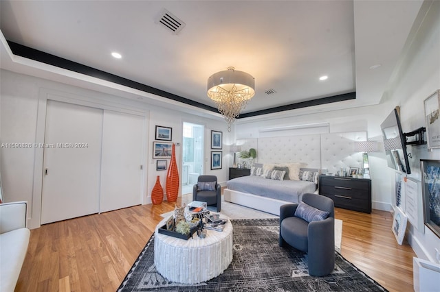 bedroom with hardwood / wood-style floors, a chandelier, and a tray ceiling