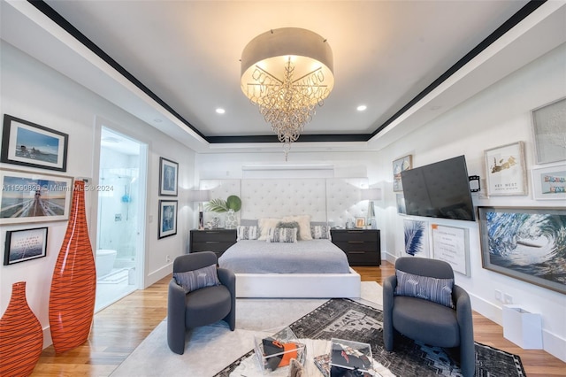 bedroom with hardwood / wood-style floors, a chandelier, connected bathroom, and a tray ceiling