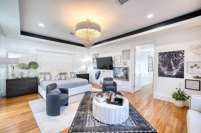 bedroom with hardwood / wood-style flooring, a tray ceiling, and a chandelier