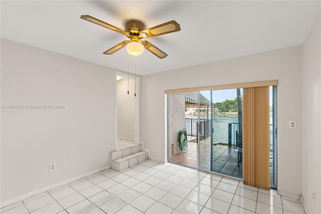 tiled spare room featuring ceiling fan and a water view