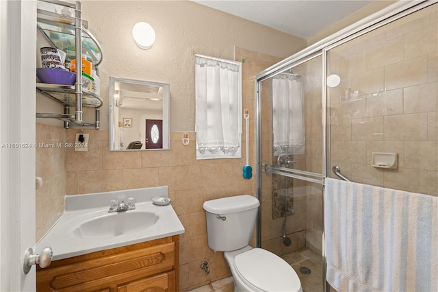 bathroom with tile walls, a shower with door, vanity, and toilet