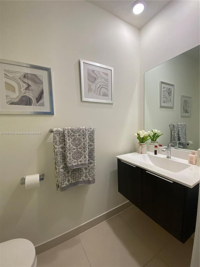 half bath featuring tile patterned flooring, vanity, toilet, and baseboards