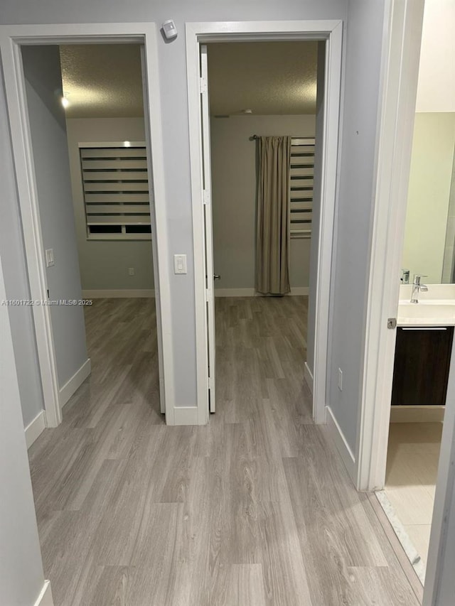 hallway featuring baseboards, a textured ceiling, a sink, and light wood-type flooring