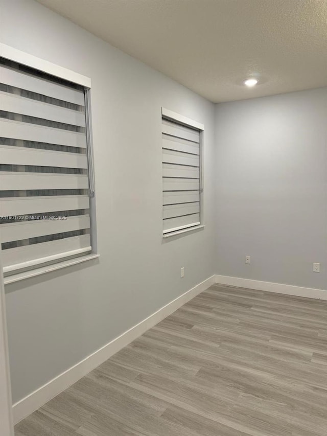 empty room with baseboards, a textured ceiling, and wood finished floors