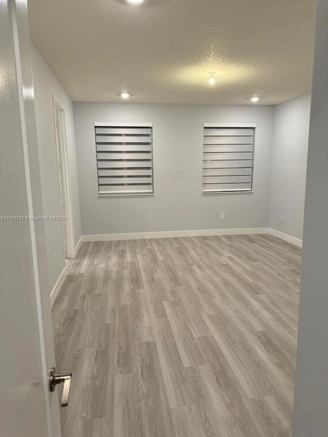 unfurnished room with a textured ceiling, baseboards, and wood finished floors