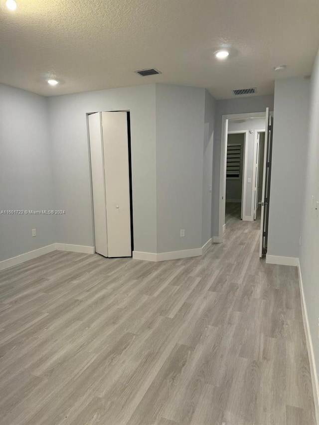 unfurnished room with light hardwood / wood-style flooring and a textured ceiling