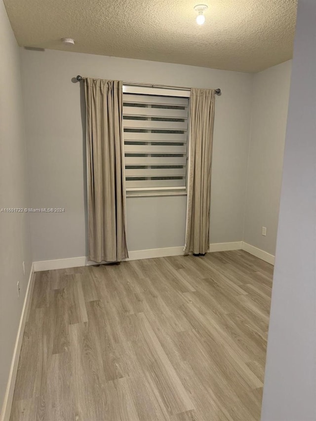 unfurnished room with a textured ceiling and light wood-type flooring