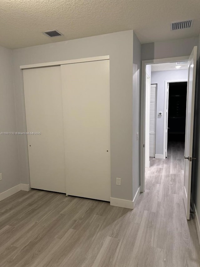 unfurnished bedroom with a closet, a textured ceiling, visible vents, baseboards, and light wood-style floors