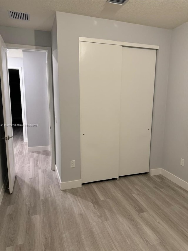 unfurnished bedroom with light wood-type flooring, a textured ceiling, and a closet