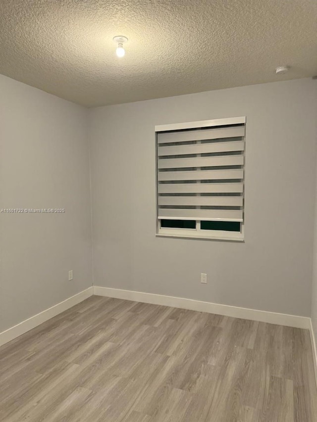 empty room with a textured ceiling, baseboards, and wood finished floors