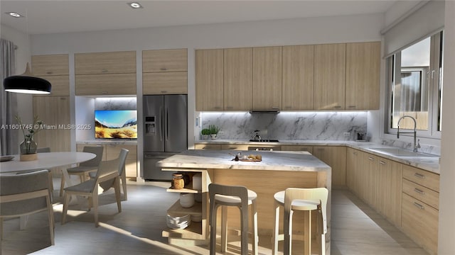 kitchen featuring sink, a kitchen island, light brown cabinetry, stainless steel fridge, and tasteful backsplash