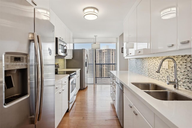 kitchen with pendant lighting, sink, appliances with stainless steel finishes, white cabinetry, and tasteful backsplash